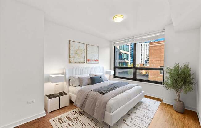 A bedroom with a large bed and a view of a cityscape through the window.