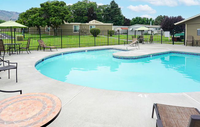 Curved outdoor pool with chairs and tables and a fence around it.at Park View Apartments, Wenatchee, WA 98801