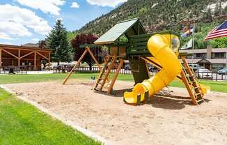 a yellow slide in a playground with a picnic shelter in the background