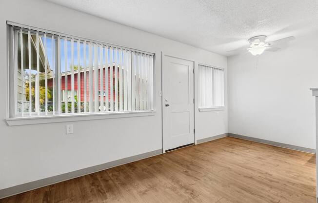 A room with a window, wooden floor, and white walls.