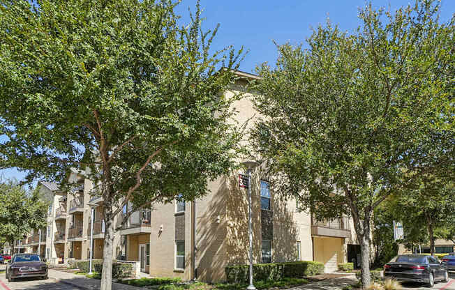 A building with a beige facade is surrounded by green trees.
