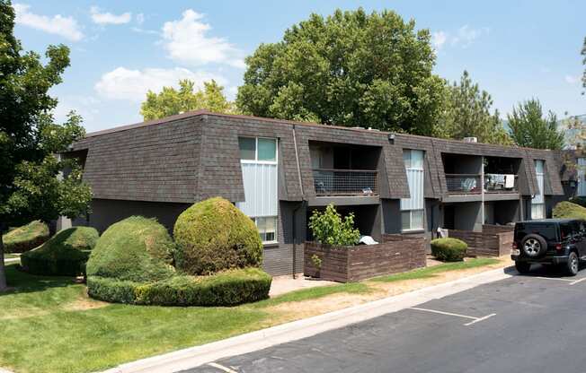A black car is parked on the street in front of a brick apartment building.
