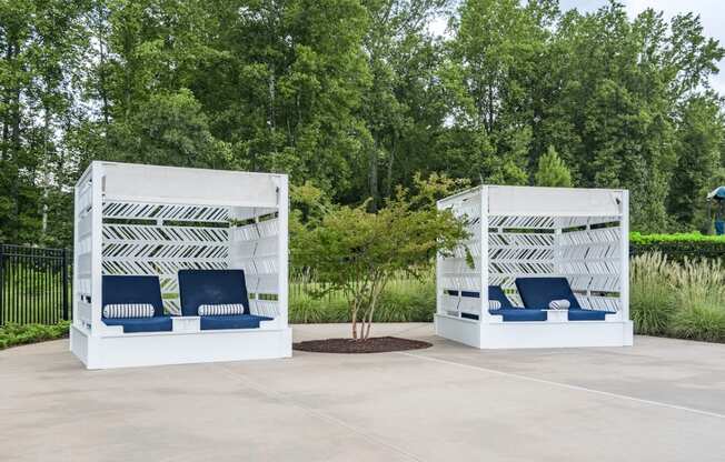 two white structures with blue chairs and a tree