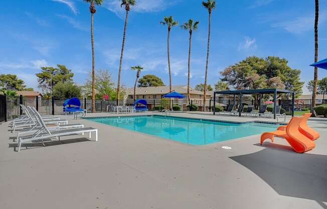 A pool surrounded by palm trees and blue umbrellas.