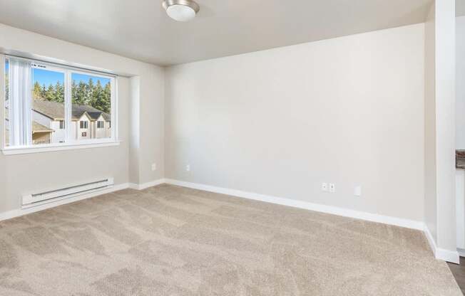 A room with a carpeted floor and a window showing a view of houses.