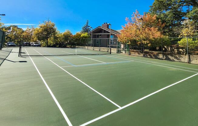 a tennis court with trees and a house in the background