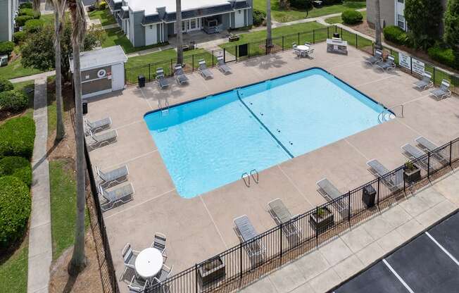 a large swimming pool with lounge chairs and tables and a building in the background