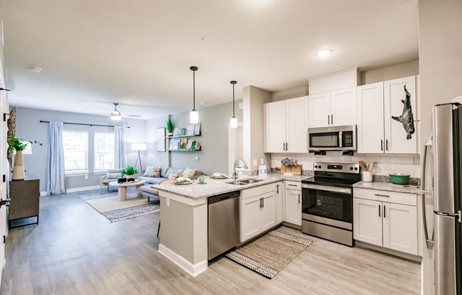an open kitchen and living room with white cabinets and stainless steel appliances