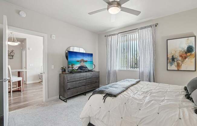 A bedroom with a large bed, a flat screen TV, and a ceiling fan.