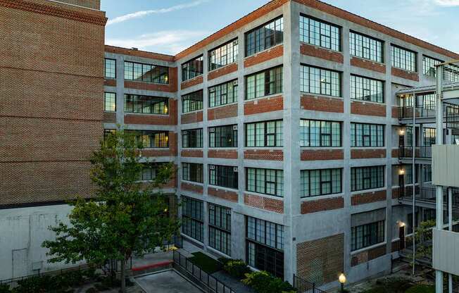A large red brick building with many windows and a tree in front.