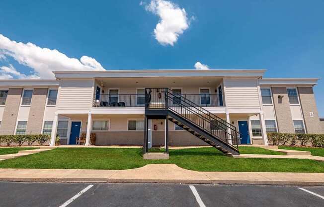 A large white apartment building with a black staircase leading to the entrance.