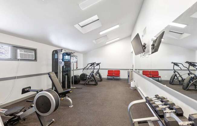 A gym with a variety of equipment including a weight bench, a rowing machine, and a treadmill.