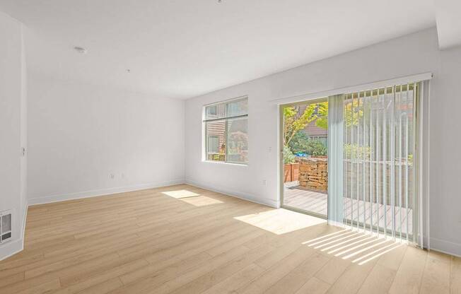 A room with wooden flooring and a window with a view of a backyard.