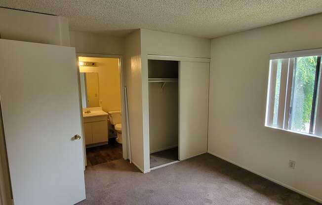 Carpeted bedroom with large window and private bathroom at Magnolia Apartments in Riverside, California.