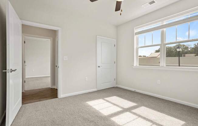A room with a ceiling fan and a large window letting in sunlight.