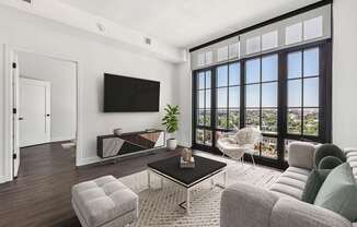 A living room with a flat screen TV mounted on the wall and a large window with a view of the city.