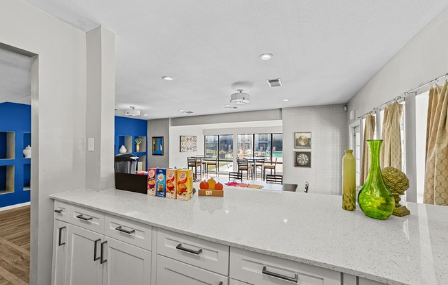 A kitchen with white cabinets and a white countertop with a green vase on it.