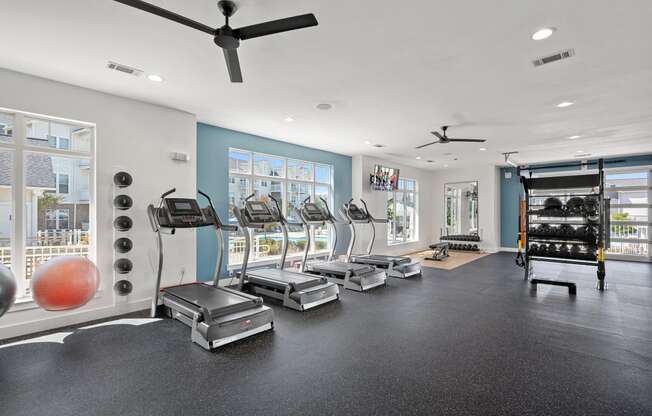 a gym with cardio machines and weights on the floor and windows