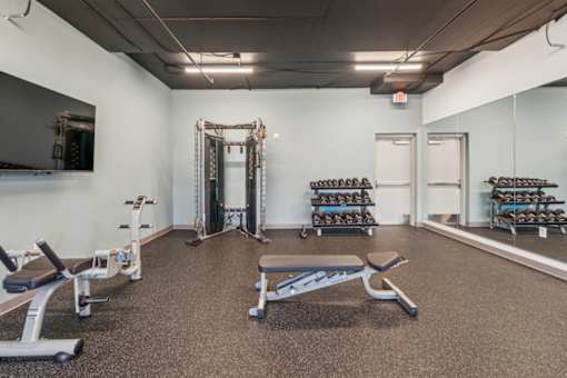 A gym with a variety of equipment including weights and benches at The Waterford At Rocketts Landing Apartments, PRG Real Estate, Richmond, Virginia