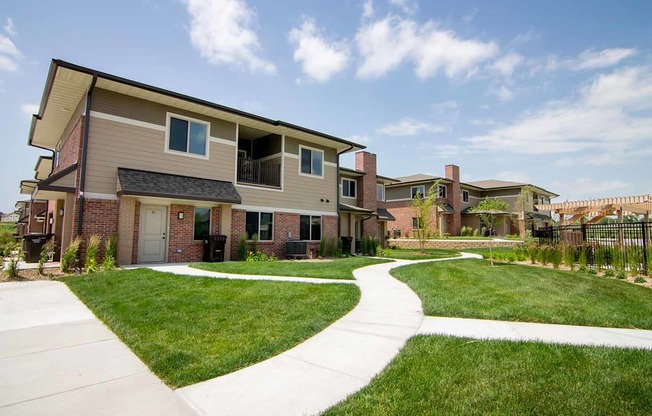 A villa-style apartment building with a green lawn in front of it, and a fenced in pool nearby.