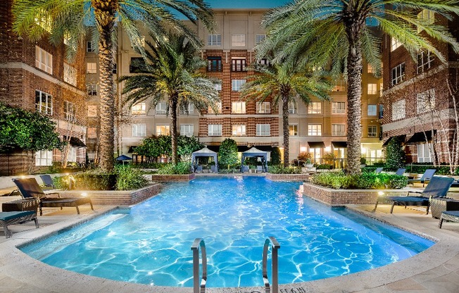 A landscaped courtyard with a large pool, lounge chairs, cabanas, and palm trees.