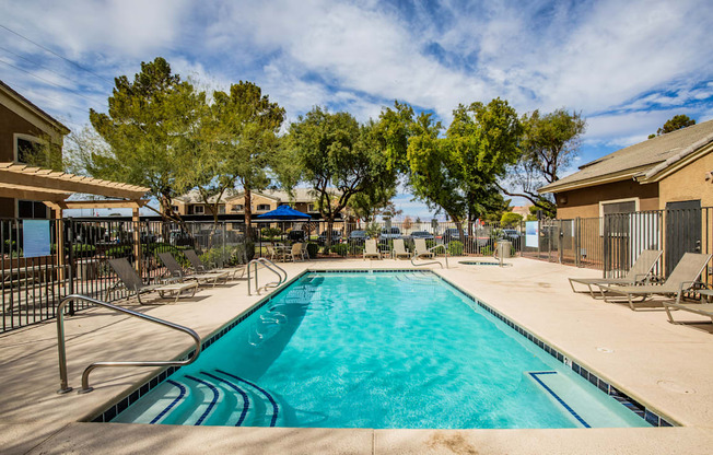 A large swimming pool with a blue tinted water surrounded by a fence and chairs.
