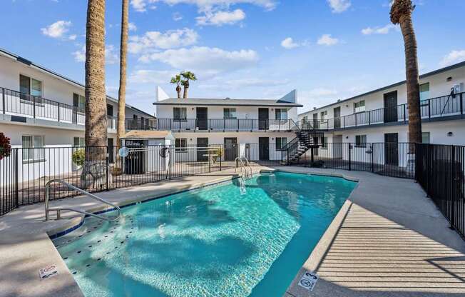 A swimming pool surrounded by palm trees and apartment buildings.