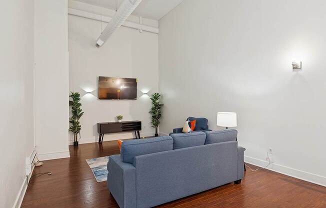 A grey couch sits in a white room with a wooden floor and a white wall.
