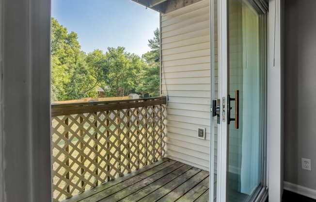 a door opens to a balcony with a view of trees and a blue sky