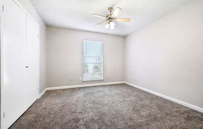 A room with a ceiling fan and a window with blinds.