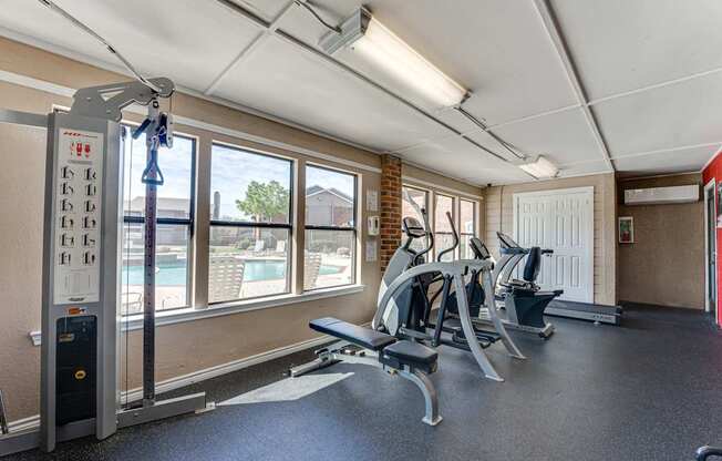 A gym with a row of exercise machines and a view of a pool outside the window.