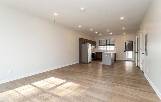 A spacious room with wooden flooring and a kitchenette in the background.