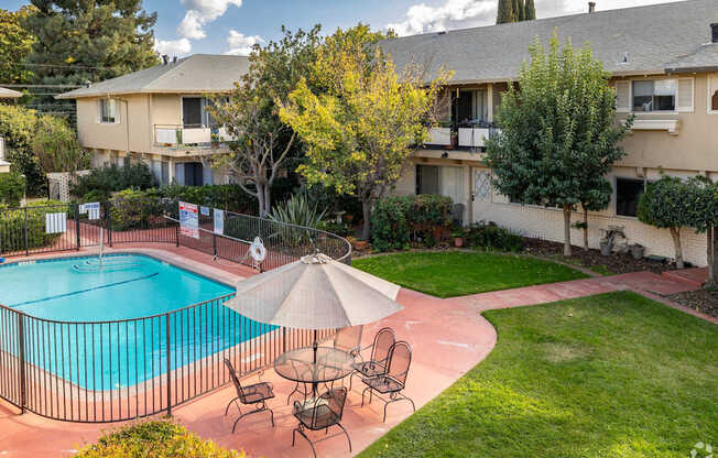 a backyard with a pool and patio with chairs and an umbrella