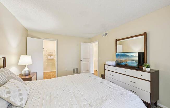 A bedroom with a large bed, a dresser with a mirror, and a lamp on a nightstand.