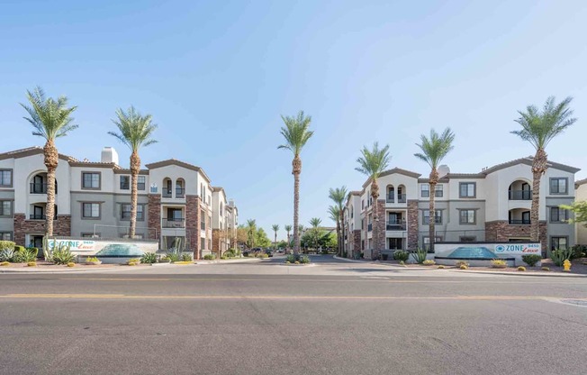 a street view of a row of apartment buildings with palm trees in the background