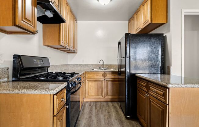 A kitchen with a black refrigerator and wooden cabinets.