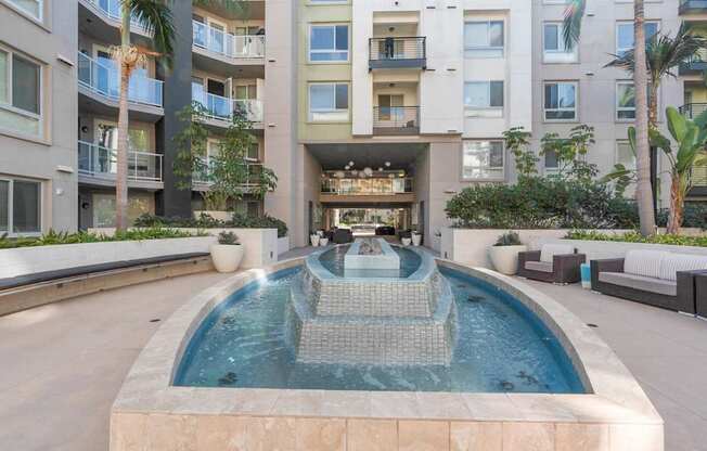 A modern pool with a waterfall in the middle of a courtyard surrounded by buildings.
