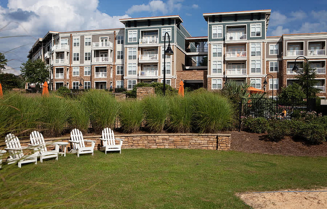 A row of white chairs are set up on a lawn in front of apartment buildings.