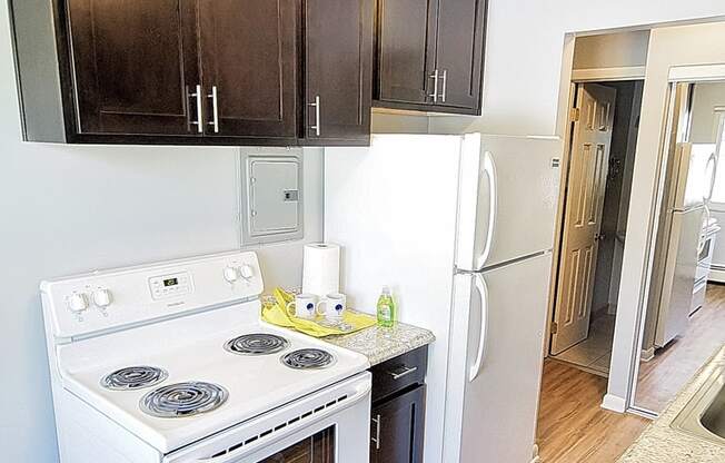 A white stove and refrigerator in a kitchen with wood floors and dark brown cabinets.