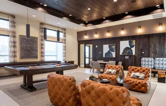 A room with a pool table and leather chairs.