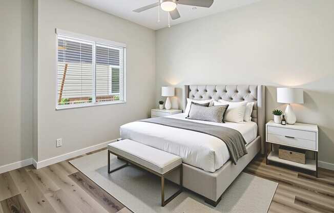A bedroom with a large bed, a ceiling fan, and a window with blinds.