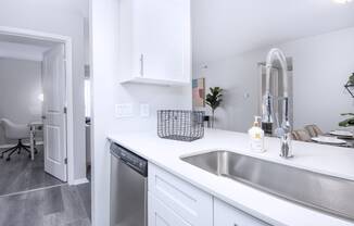 a kitchen with a sink and a dishwasher and a door to a living room