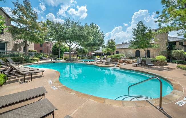 A large outdoor swimming pool surrounded by lounge chairs and trees.