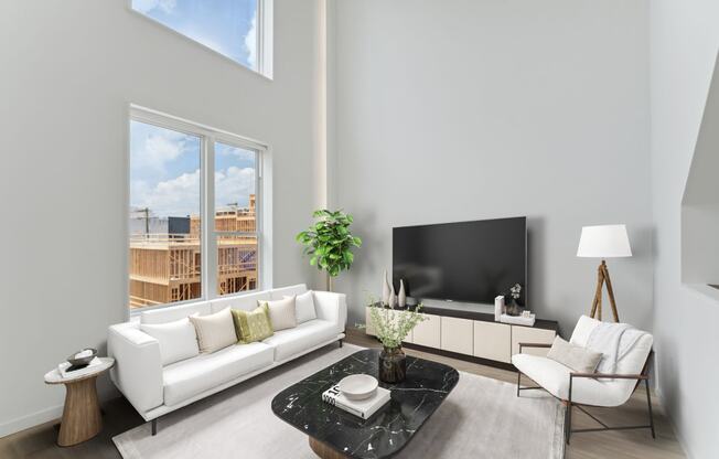 Spacious living room with high ceilings, featuring a sleek white sofa, contrasting black armchairs, and a view of the construction outside through large windows.