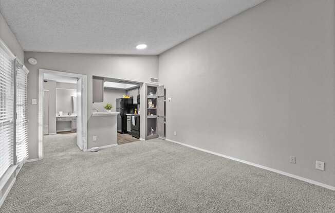 A spacious room with a carpeted floor and a kitchen area visible through the open door.