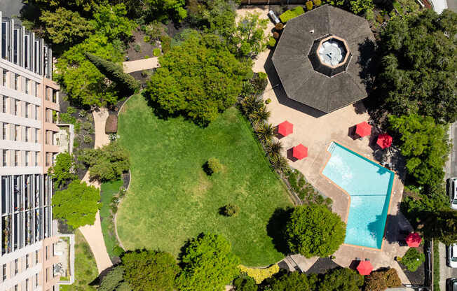 A large building is to the left of a green area with a pool and a pavilion.