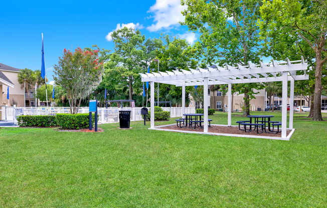 A white pergola with benches is situated in a grassy area.