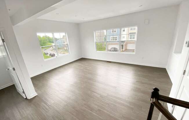 A spacious room with a wooden floor and a view of a parking lot through the windows.