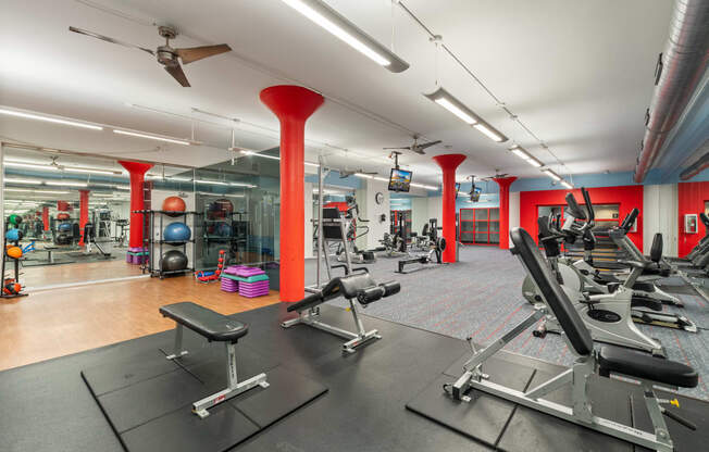 a gym with cardio equipment and weights on the floor and red pillars