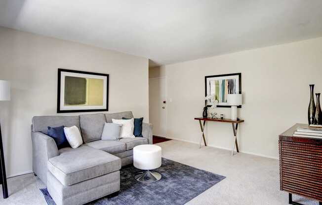 A grey couch with a white ottoman in front of a painting.